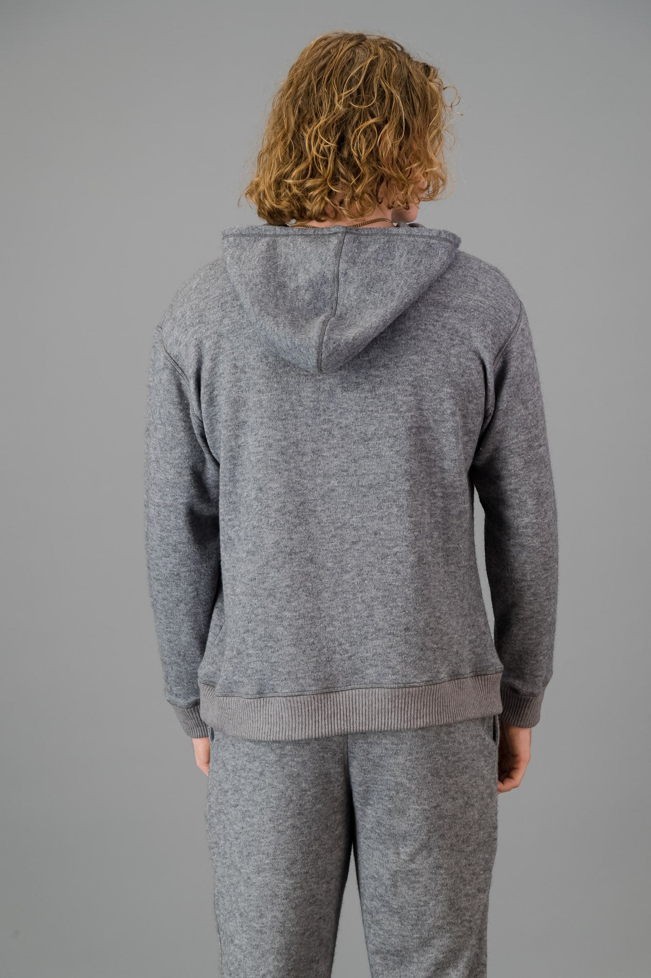 Person with curly blonde hair wearing a comfortable Cashmere-Feel Hoodie (Grey) and matching relaxed fit grey joggers.