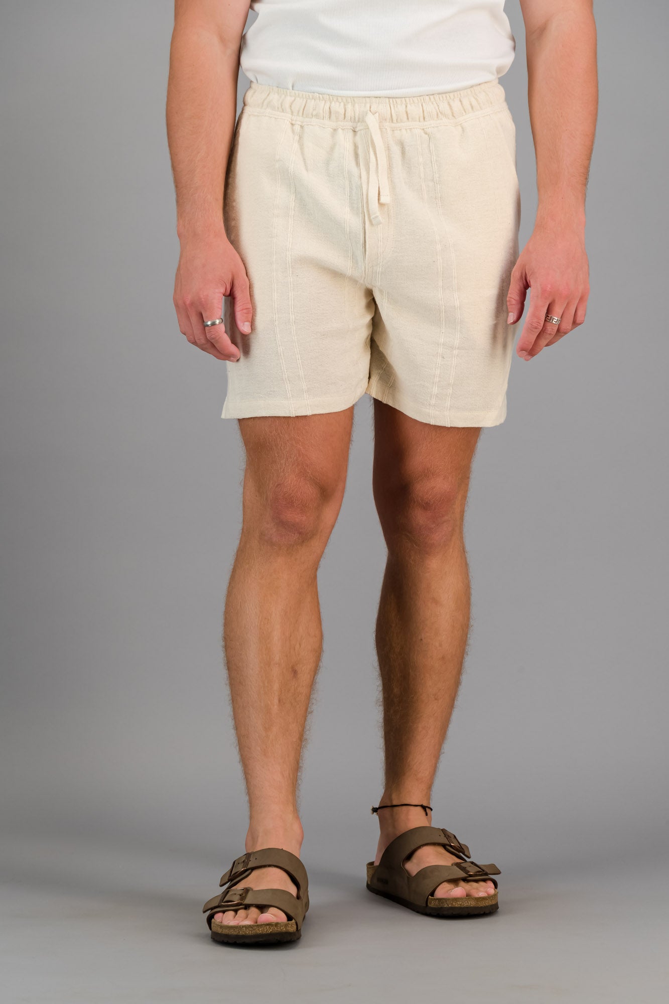 A man wearing cream cotton cord shorts with a white vest.