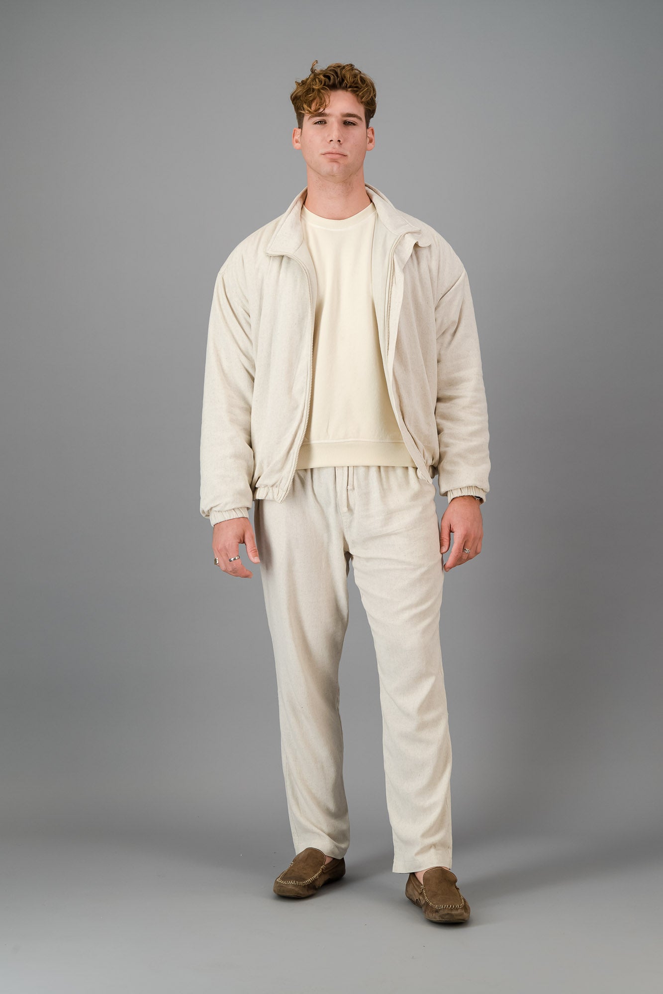 A man stands against a gray background, wearing a stylish and cozy Oatmeal Linen Viscose Bomber and matching pants, looking directly at the camera.