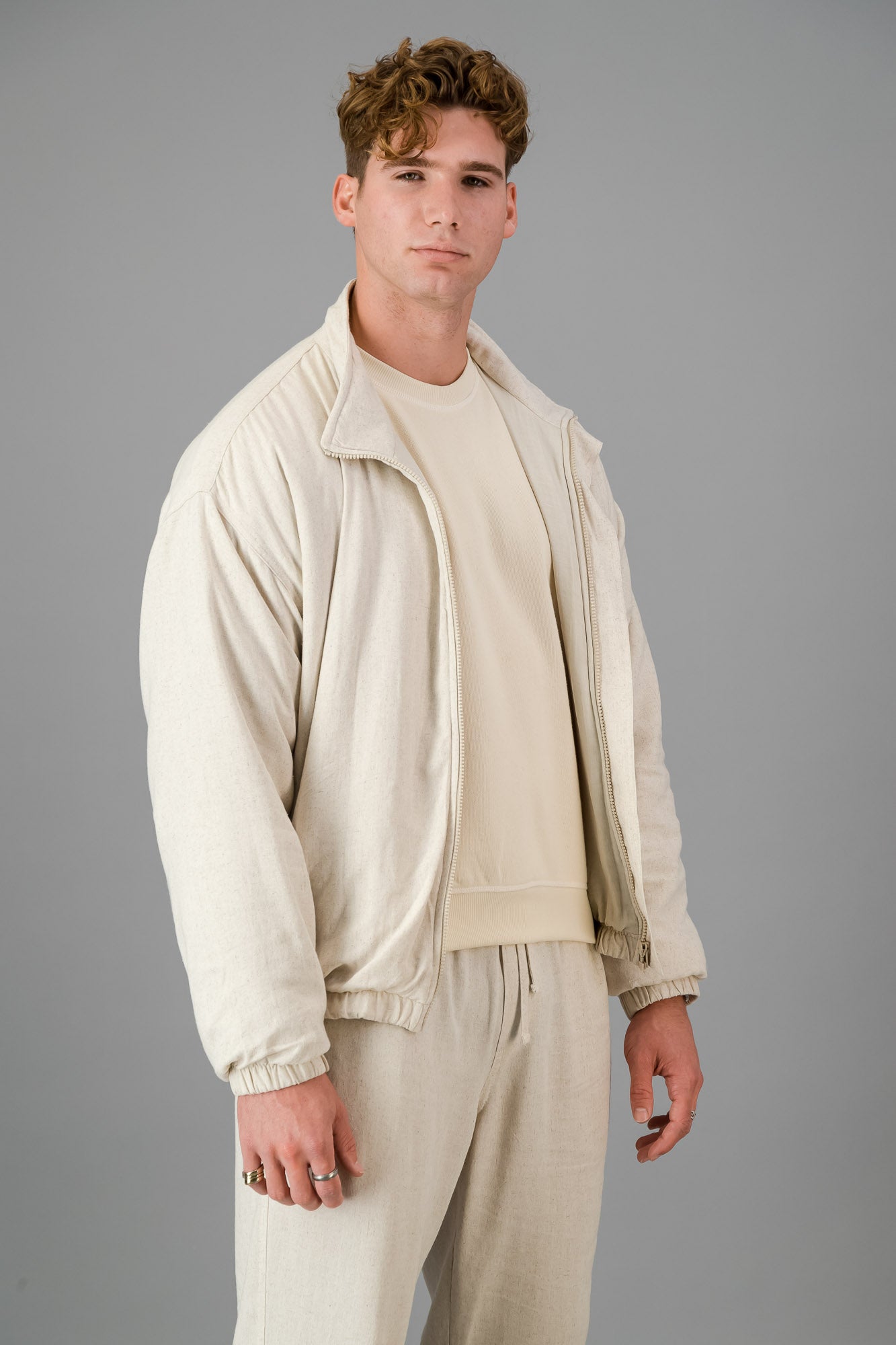 A man stands against a gray background, wearing a stylish and cozy Oatmeal Linen Viscose Bomber and matching pants, looking directly at the camera.