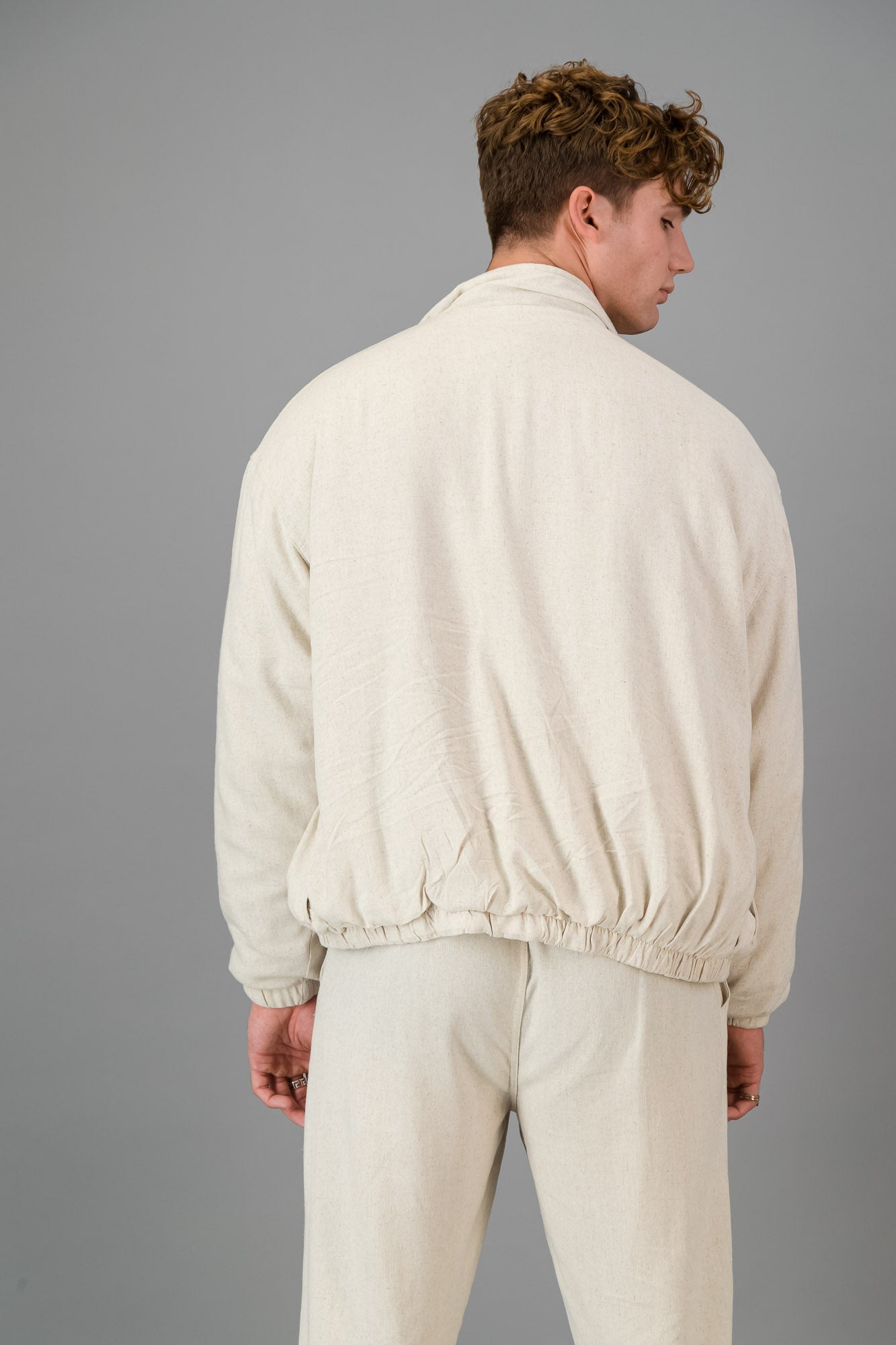 A man stands against a gray background, wearing a stylish and cozy Oatmeal Linen Viscose Bomber and matching pants, looking directly at the camera.