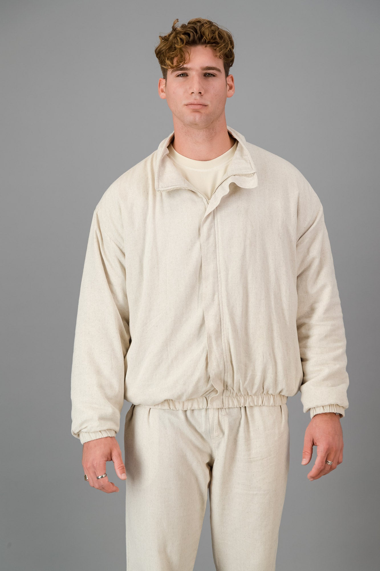 A man stands against a gray background, wearing a stylish and cozy Oatmeal Linen Viscose Bomber and matching pants, looking directly at the camera.