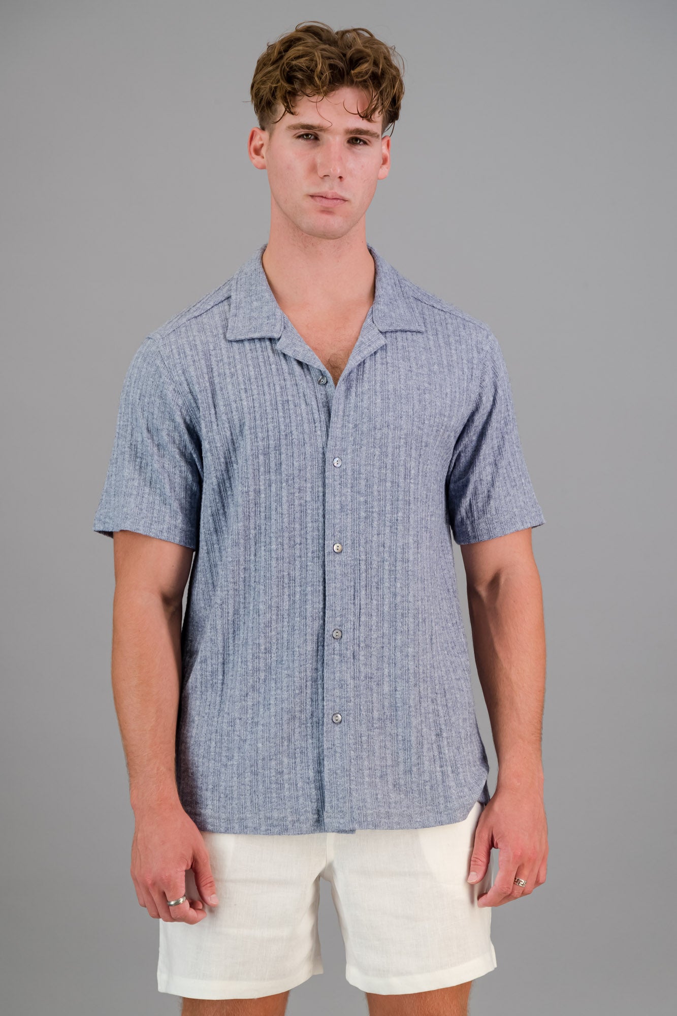 Model wearing a Rayon-rich Cable Knit Shirt in blue and white linen shorts.