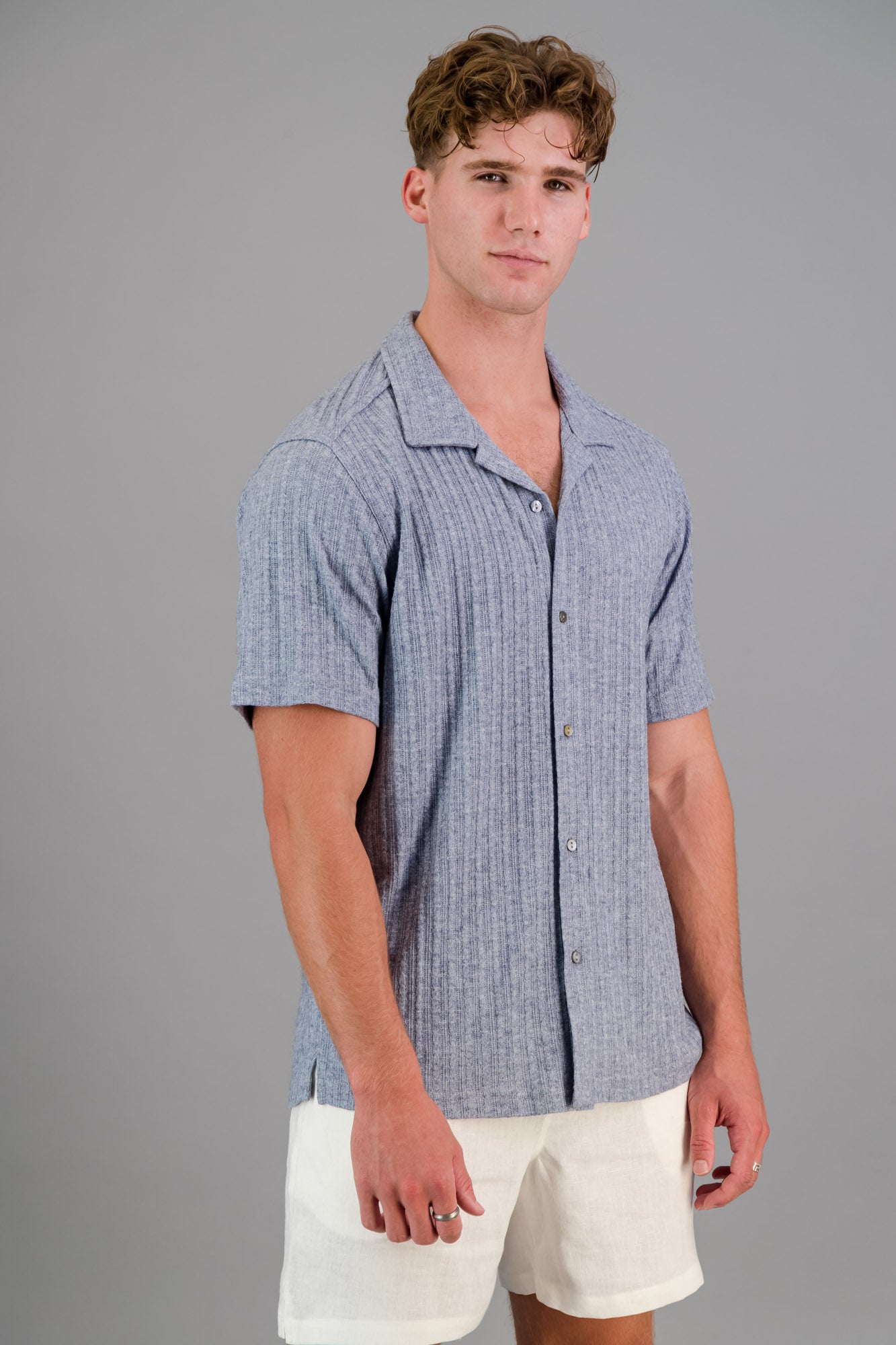 Model wearing a Rayon-rich Cable Knit Shirt in blue and white linen shorts.