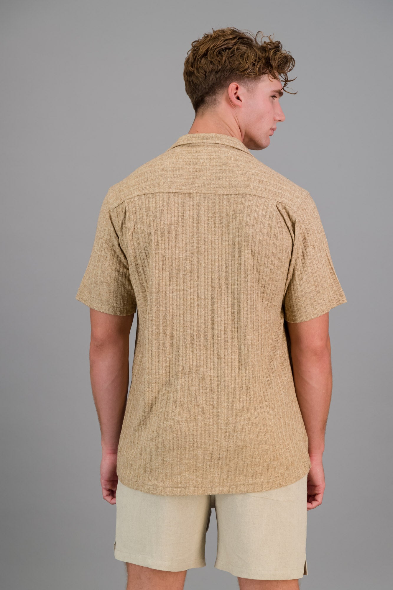 Model wearing a short-sleeve Rayon-rich Cable Knit Shirt in brown and oatmeal shorts.