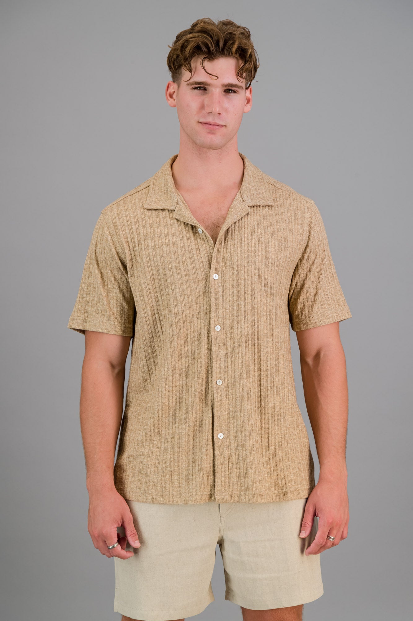 Model wearing a short-sleeve Rayon-rich Cable Knit Shirt in brown and oatmeal shorts.