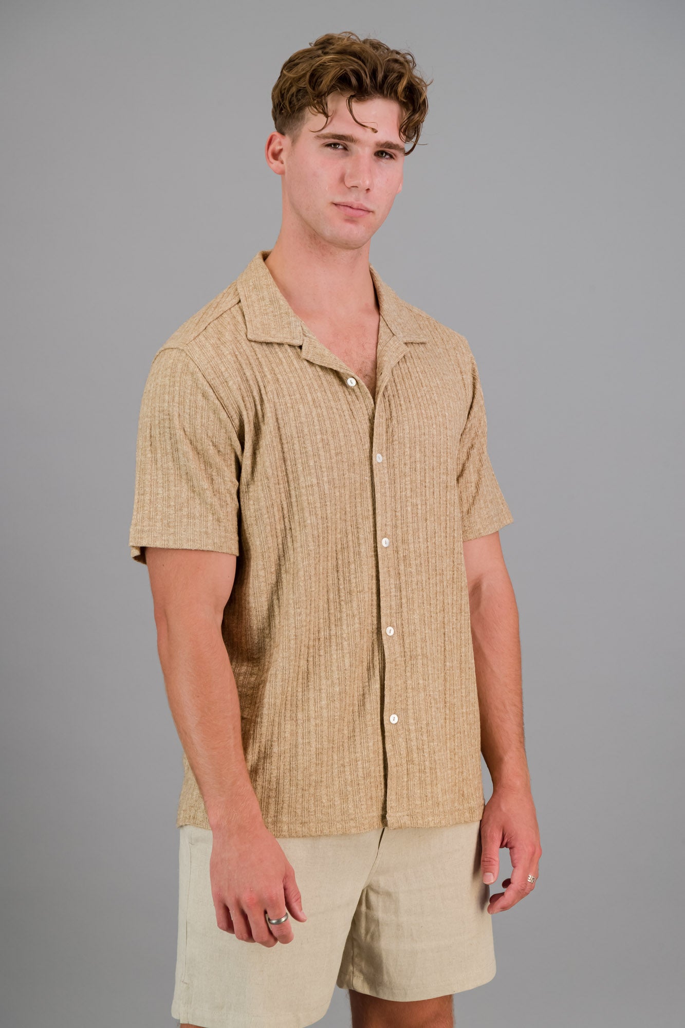 Model wearing a short-sleeve Rayon-rich Cable Knit Shirt in brown and oatmeal shorts.