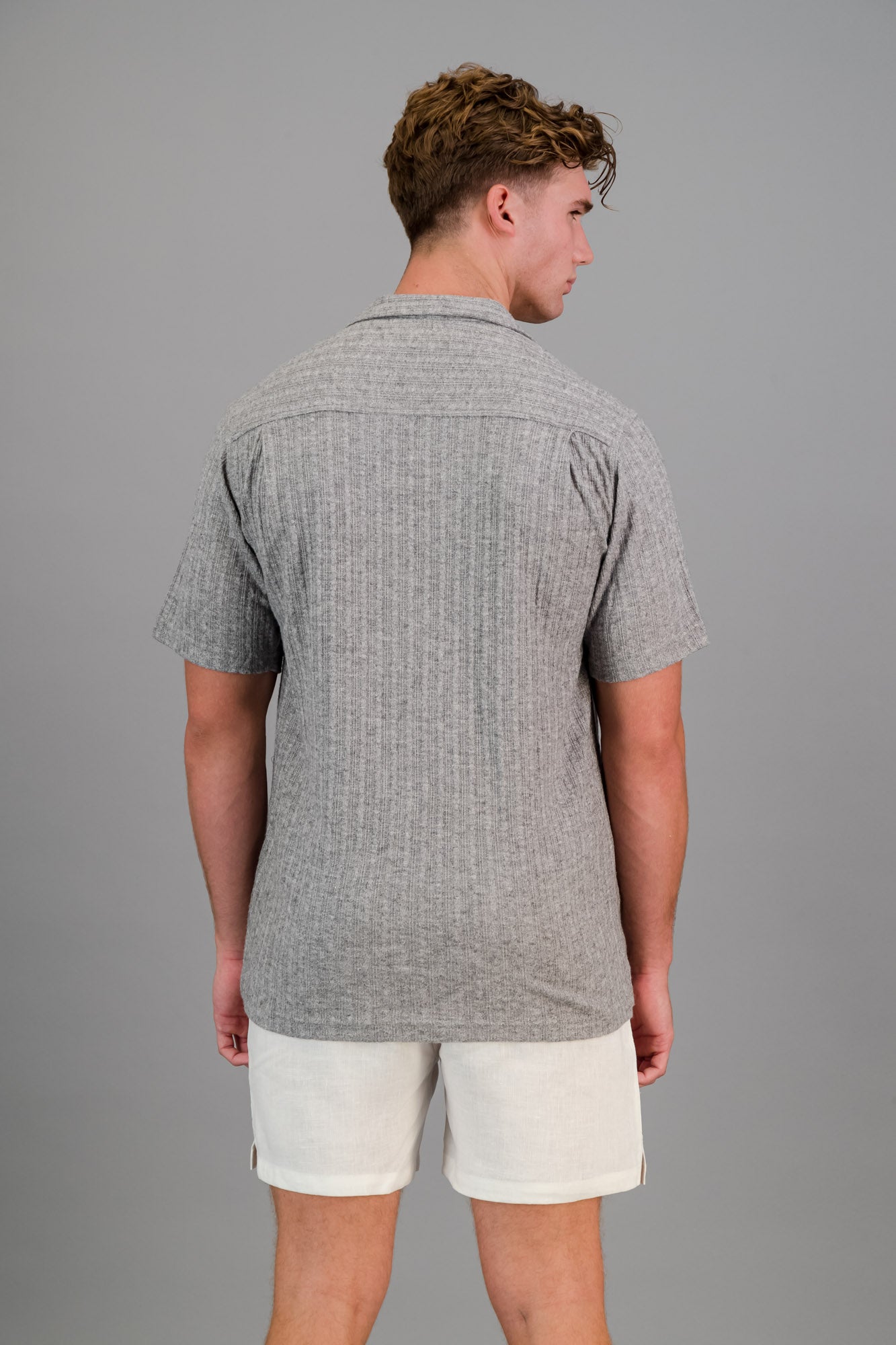 Model wearing a short-sleeve Rayon-rich Cable Knit Shirt in Grey and white linen shorts.