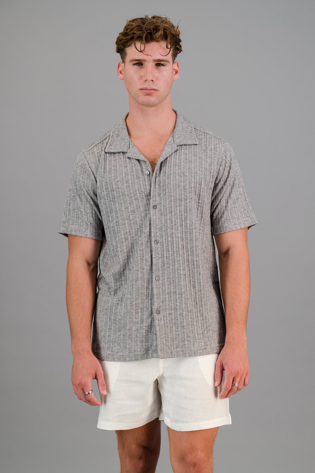 Model wearing a short-sleeve Rayon-rich Cable Knit Shirt in Grey and white linen shorts.