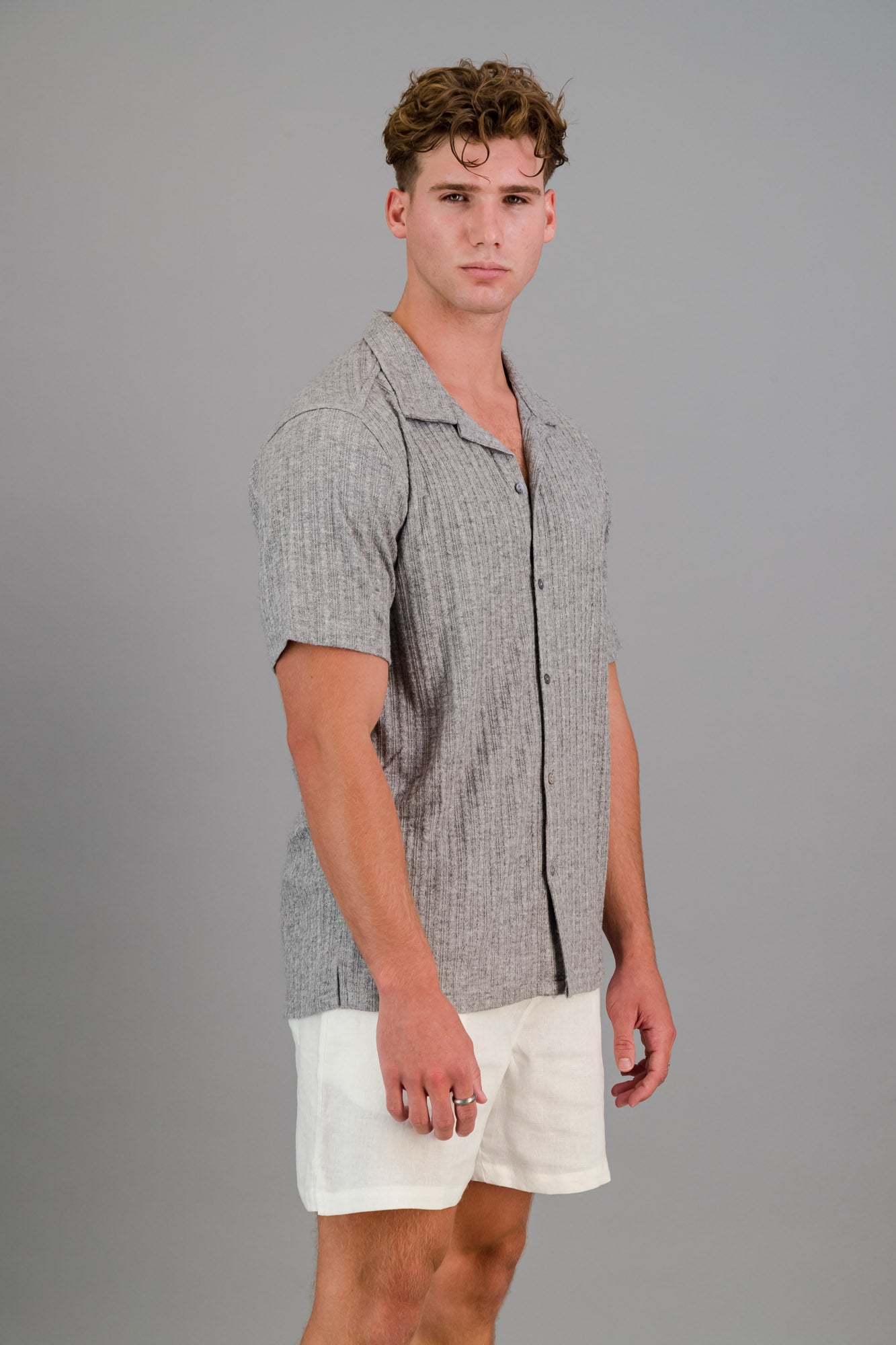 Model wearing a short-sleeve Rayon-rich Cable Knit Shirt in Grey and white linen shorts.