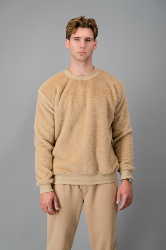 A man clad in a luxurious Caramel Fur Crew Neck Sweater, with matching pants, stands against a gray background gazing at the camera.